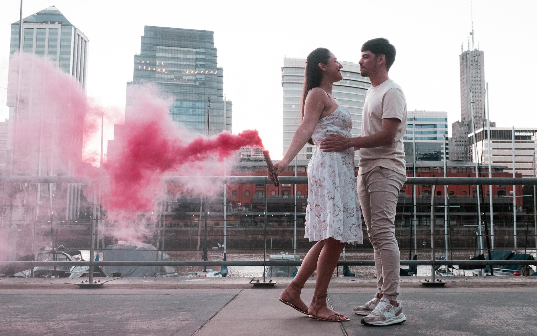A couple embraces with a vibrant red smoke bomb in Buenos Aires, creating a romantic urban scene.