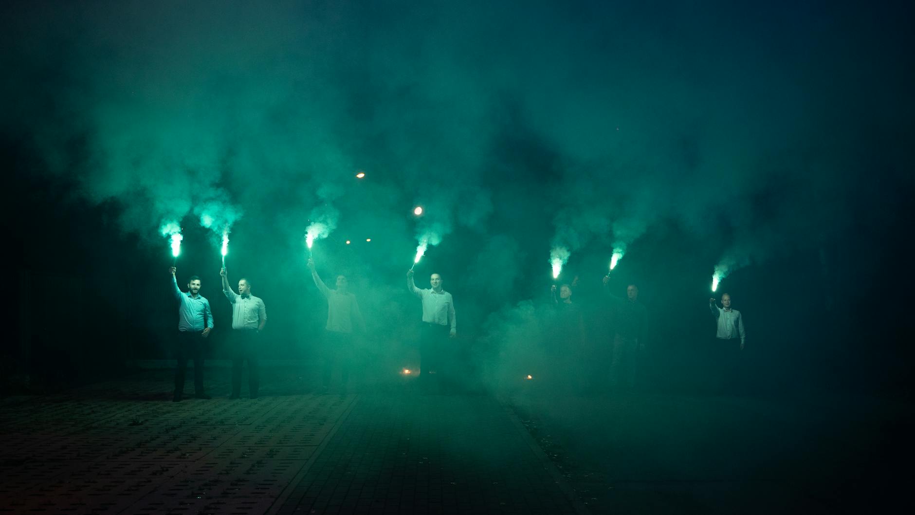 A group of men holding smoke flares, creating an ethereal night scene with colorful smoke.