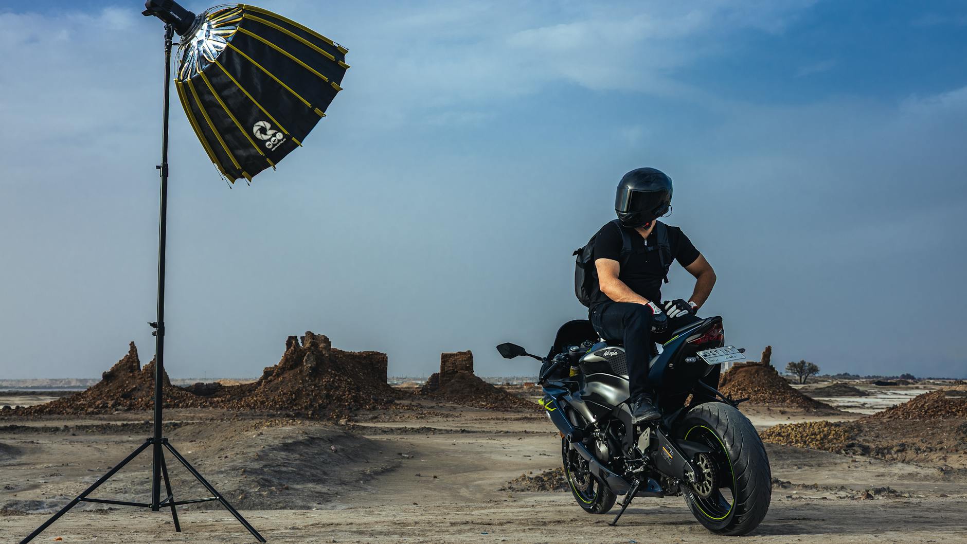 Rider on sport motorcycle in desert with lighting setup, ready for a photoshoot.