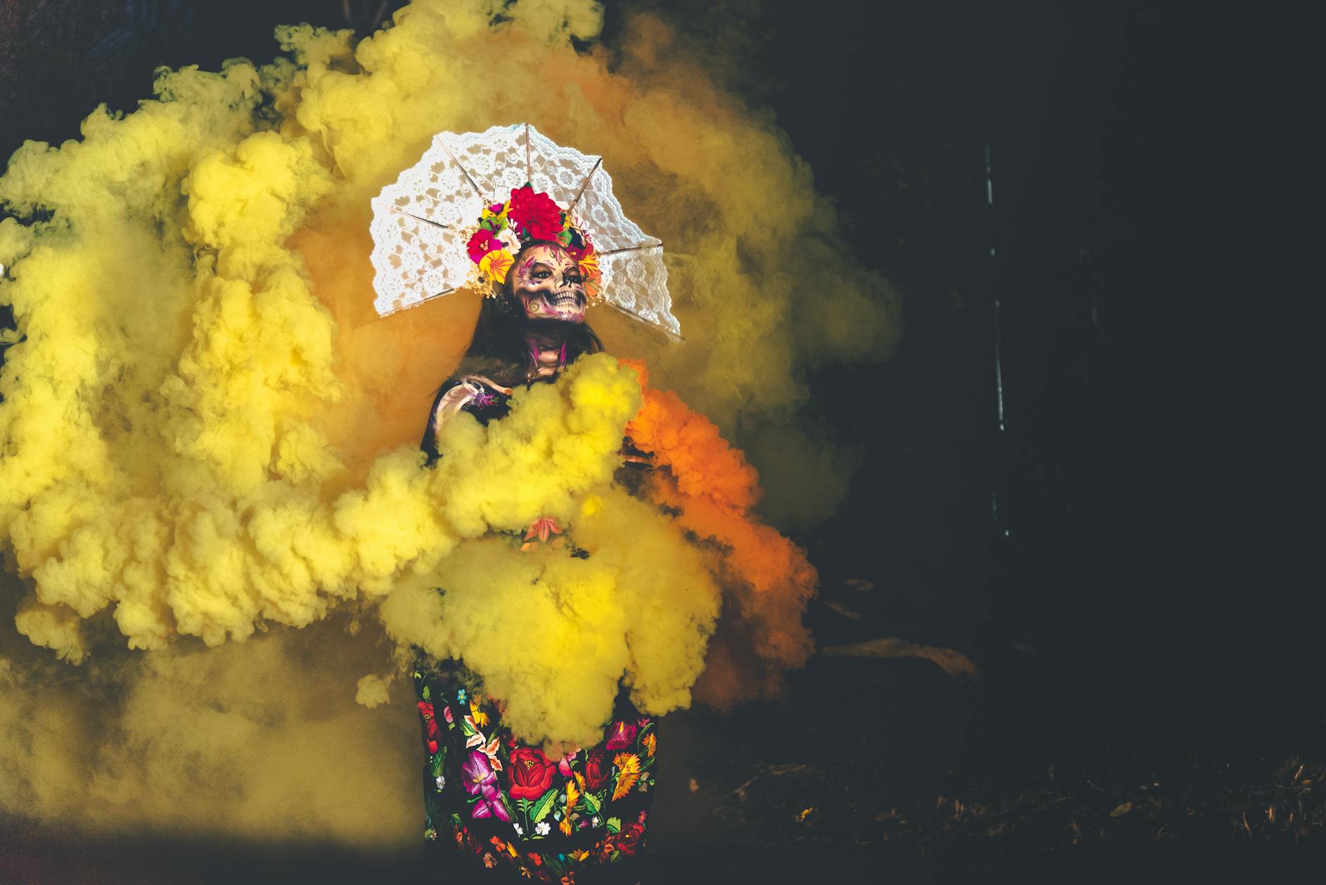 Colorful Day of the Dead scene featuring a woman with traditional makeup and costume amidst vibrant smoke.