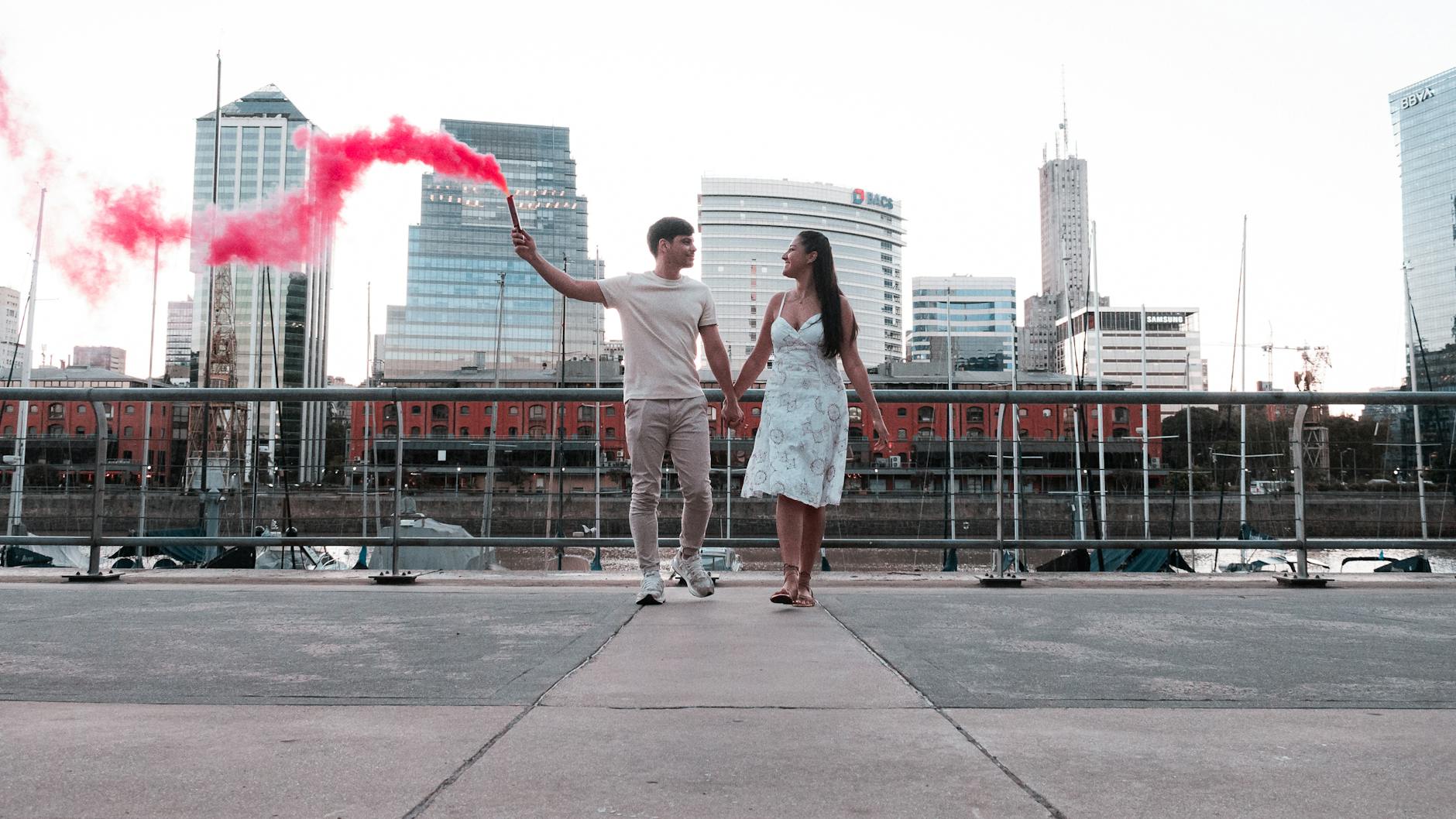 Romantic couple holding a red smoke bomb at a riverside in Buenos Aires, Argentina.