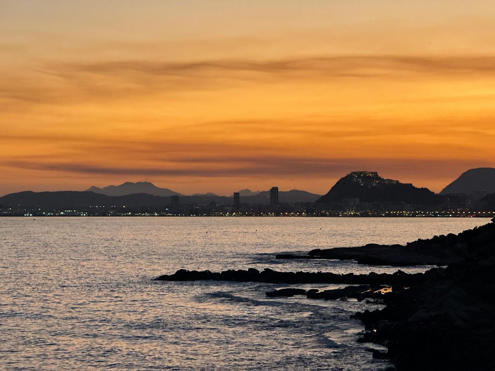 Beautiful sunset view over the Alicante coastline with city lights and mountain silhouette.