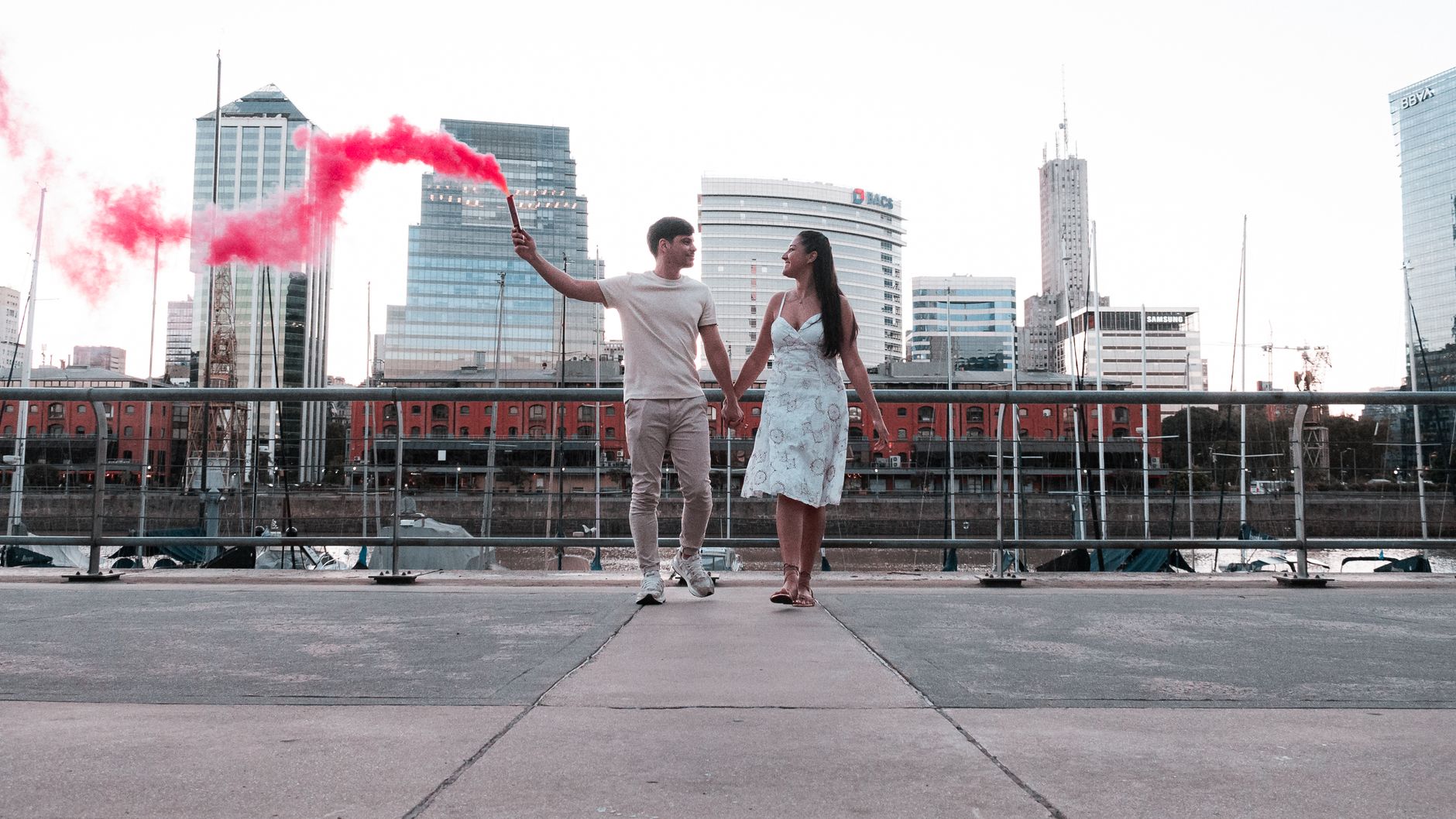 Romantic couple holding a red smoke bomb at a riverside in Buenos Aires, Argentina.