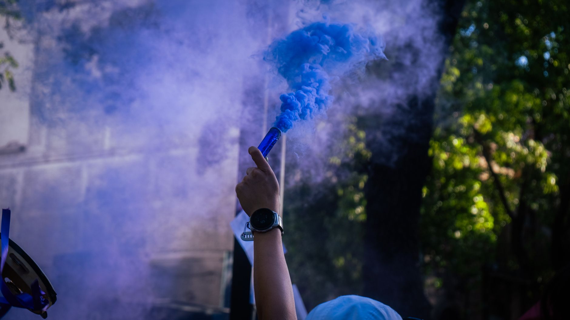A hand holding a blue smoke flare, creating vibrant smoke in an outdoor setting.