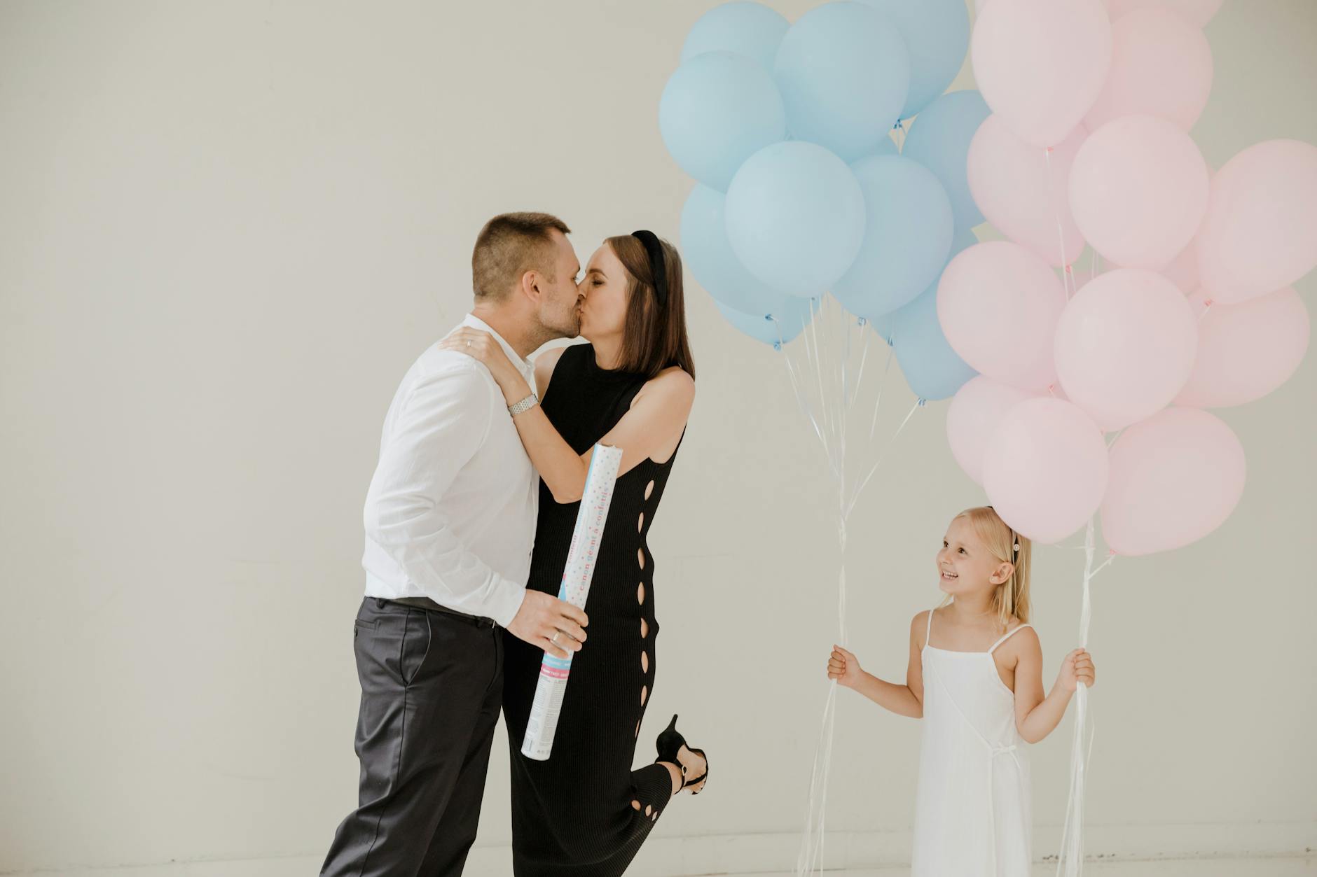 Family celebrating a gender reveal with balloons and a joyful kiss.