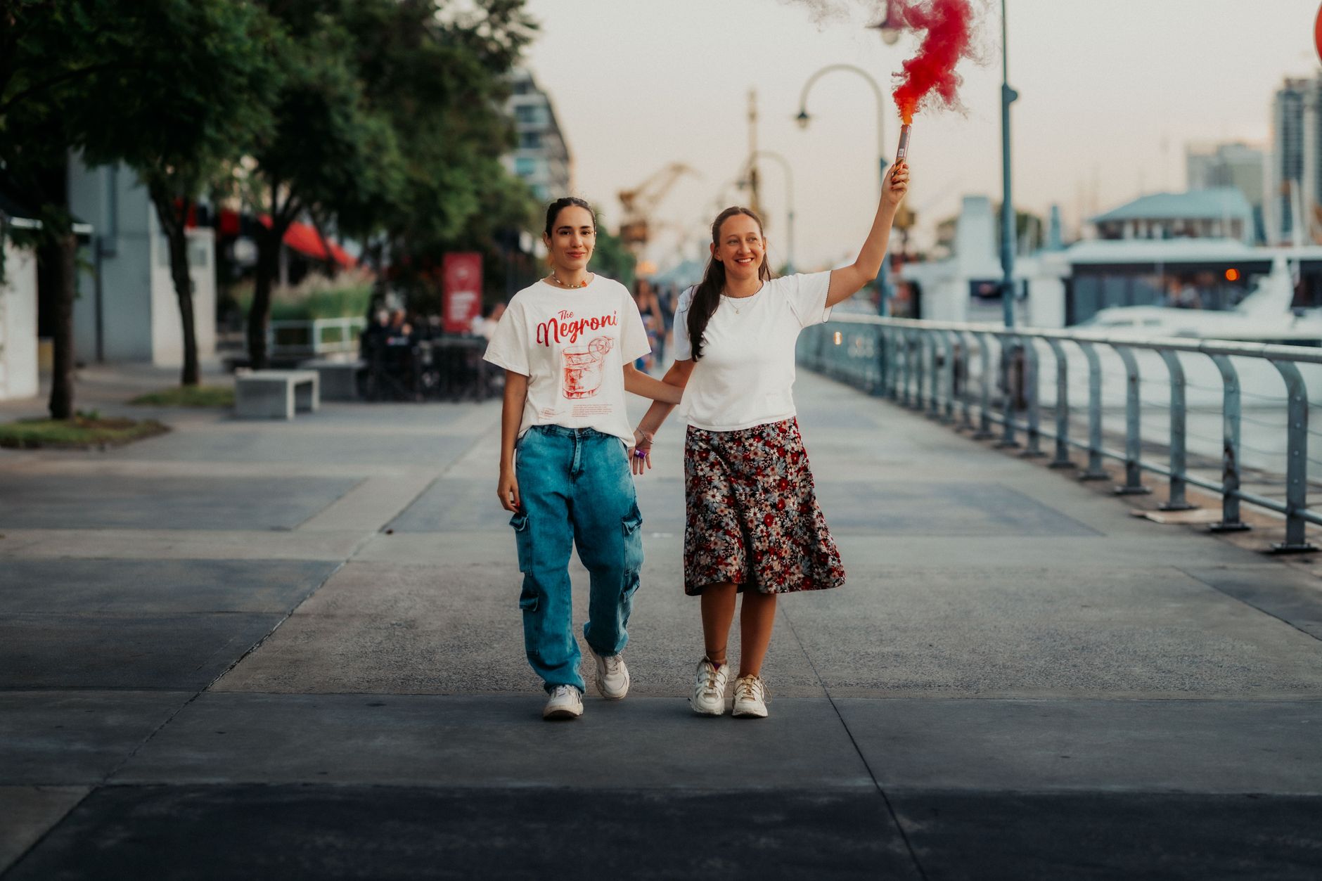A joyful couple walks on the Buenos Aires waterfront, celebrating with a smoke flare.