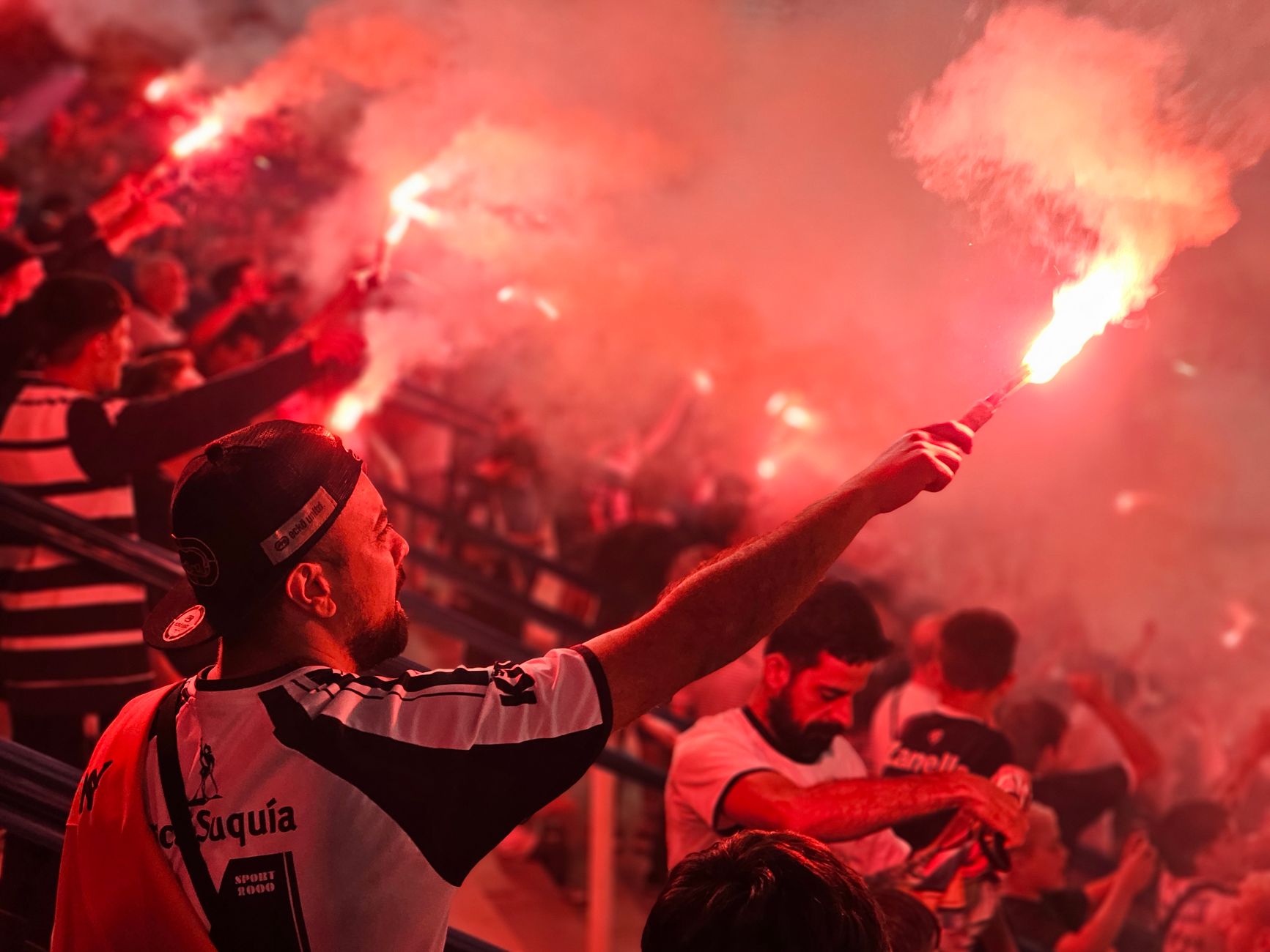 Energetic crowd celebrating with red flares at a sports event, creating a vibrant and passionate atmosphere.