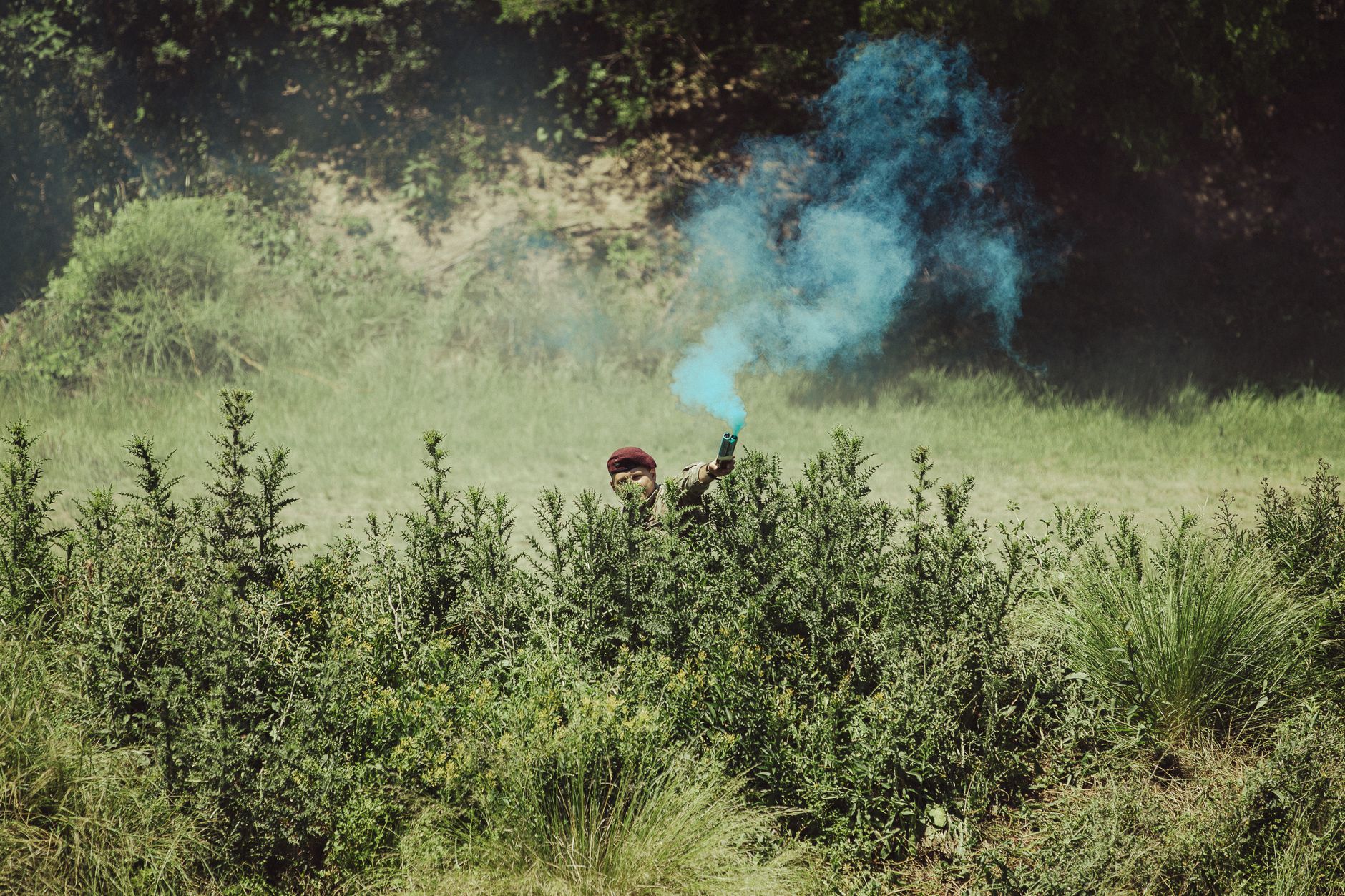 A soldier uses a blue smoke signal in a grassy field during military training in Argentina.
