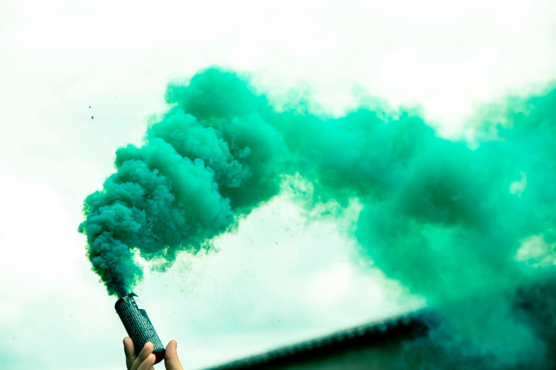 Low angle of crop anonymous person demonstrating bright smoke bomb against clear sky