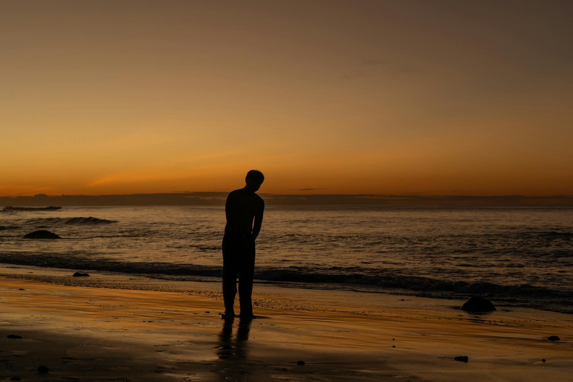 A silhouette of a person standing on a beach during a breathtaking sunset.