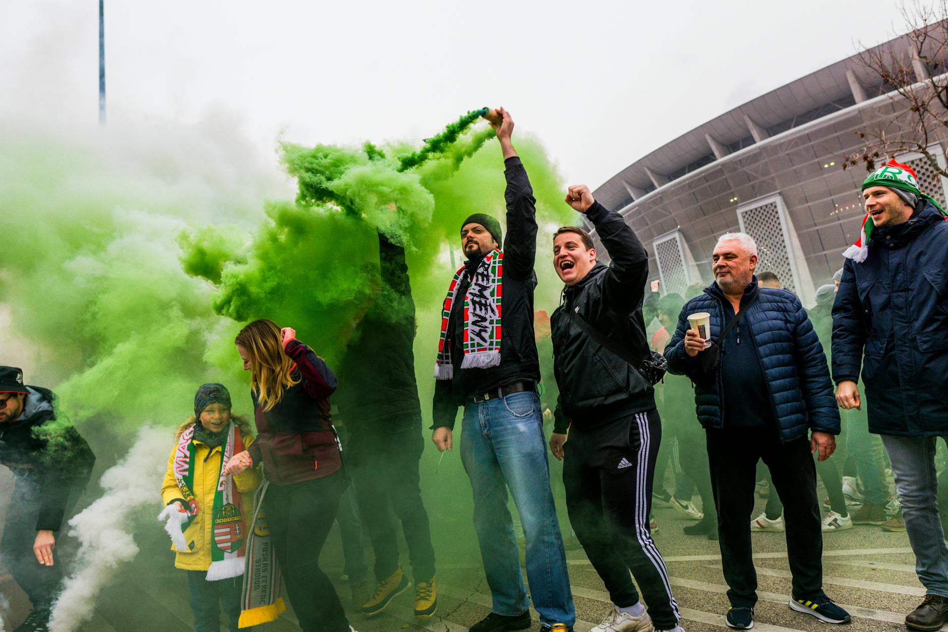 Group of enthusiastic sports fans lighting green smoke flares outside a stadium in Budapest, Hungary.