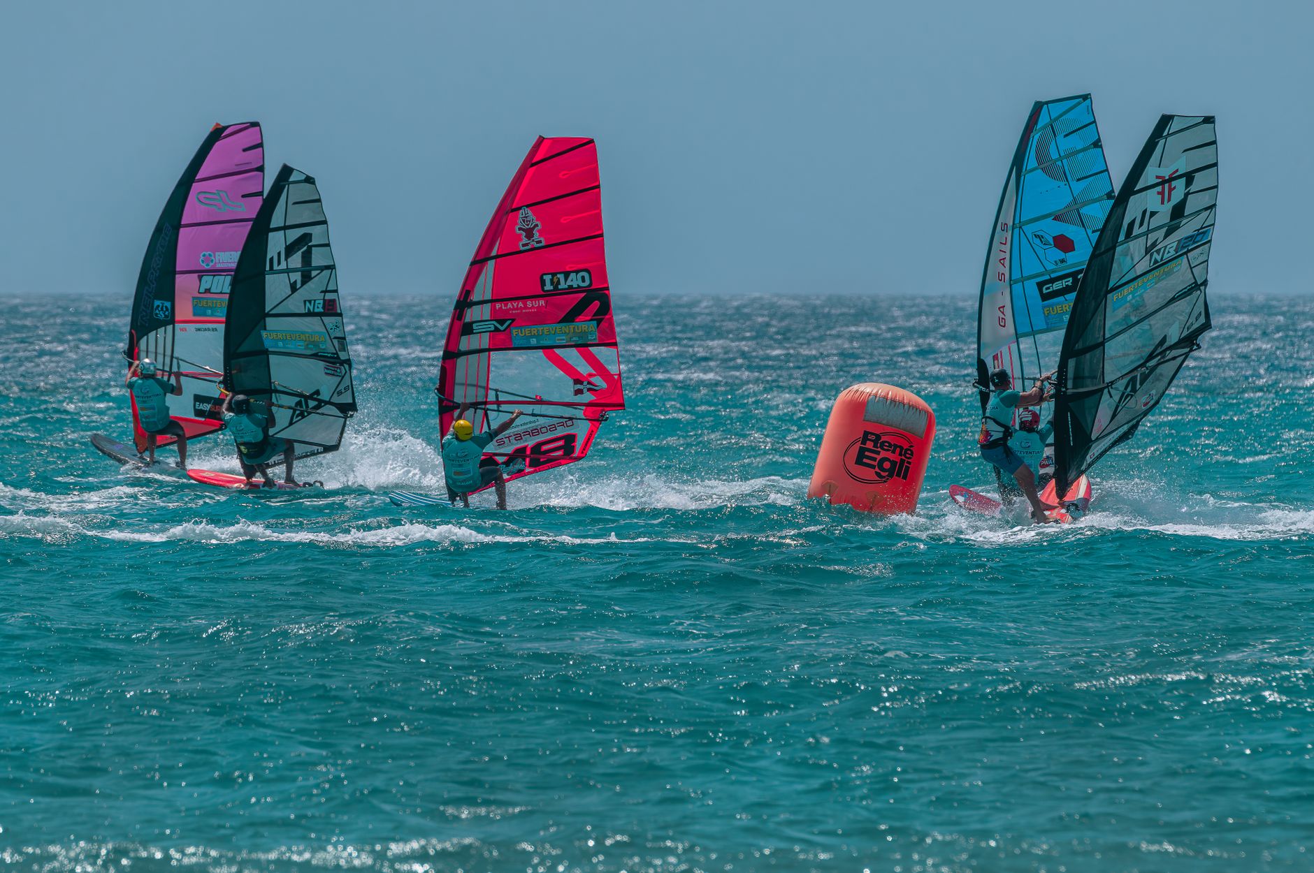 Windsurfers race across vibrant blue waters in Canarias, España under bright skies.