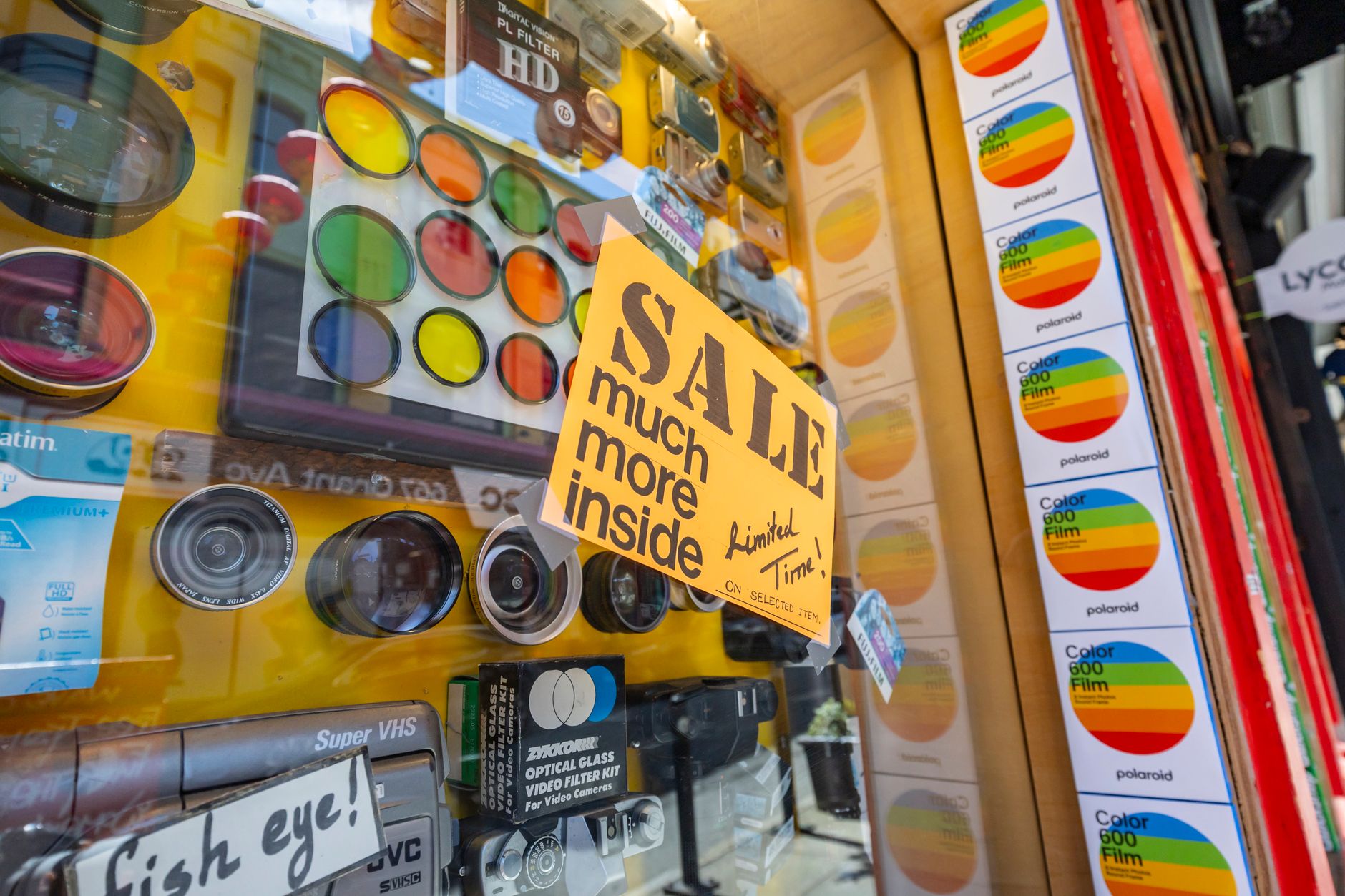 Vibrant display of camera lenses and accessories with a sale sign in a shop window.