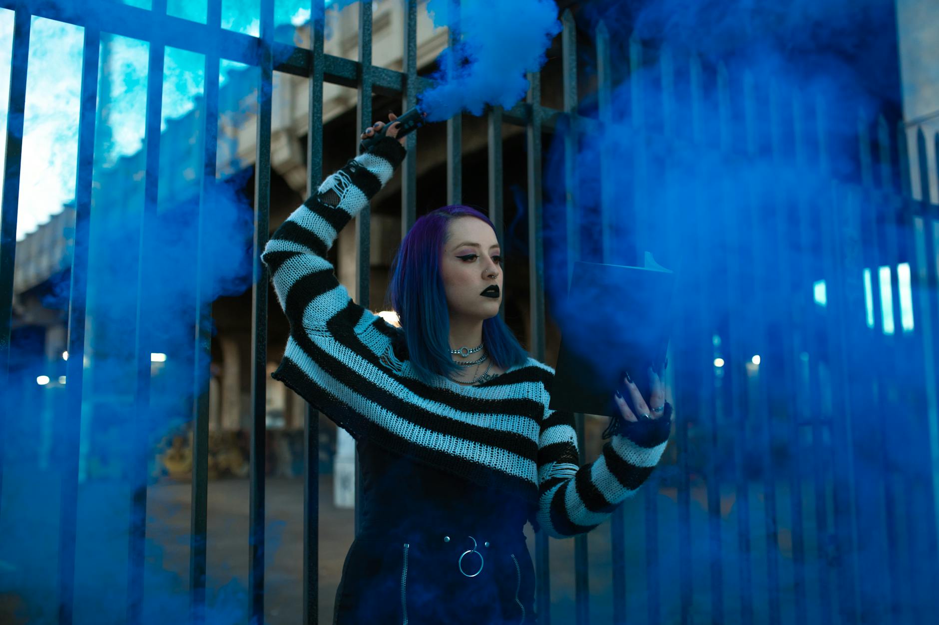 Young woman in urban setting with smoke bomb and striped sweater, expressing modern youth culture.