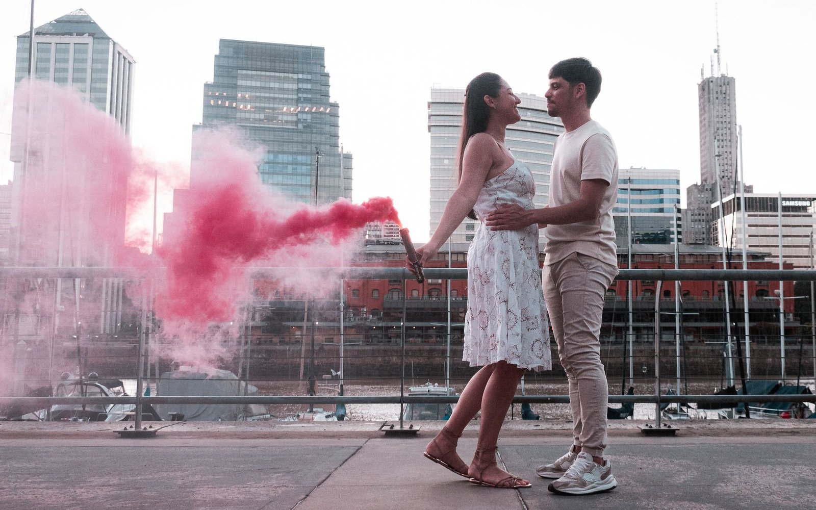 A couple embraces with a vibrant red smoke bomb in Buenos Aires, creating a romantic urban scene.