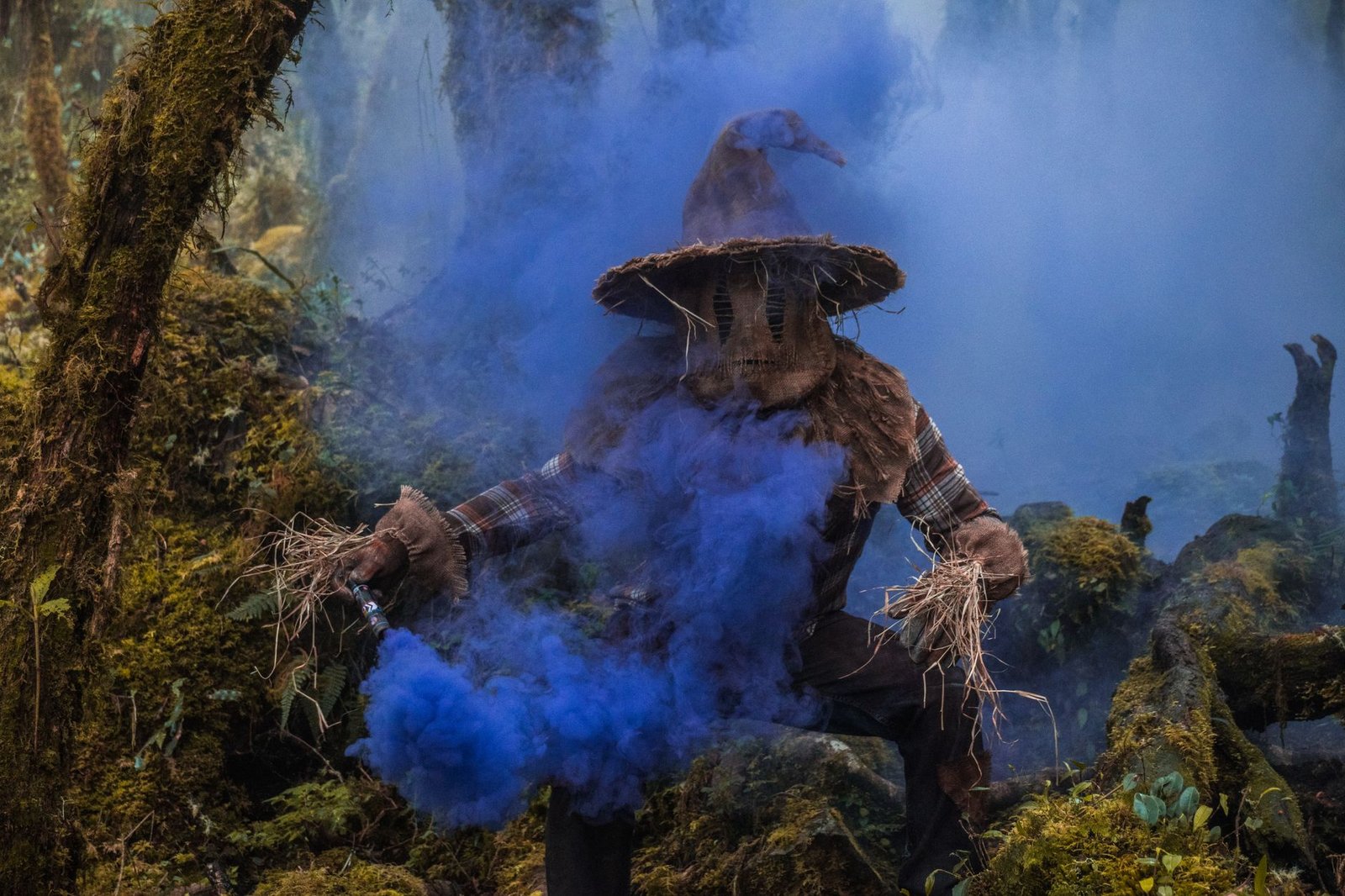 A scarecrow surrounded by blue smoke in a foggy forest sets a chilling Halloween atmosphere.