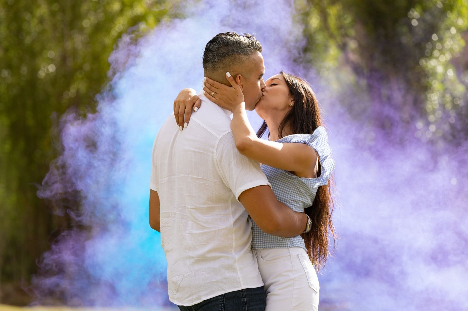 A couple passionately kissing amidst vibrant purple smoke in a lush park.