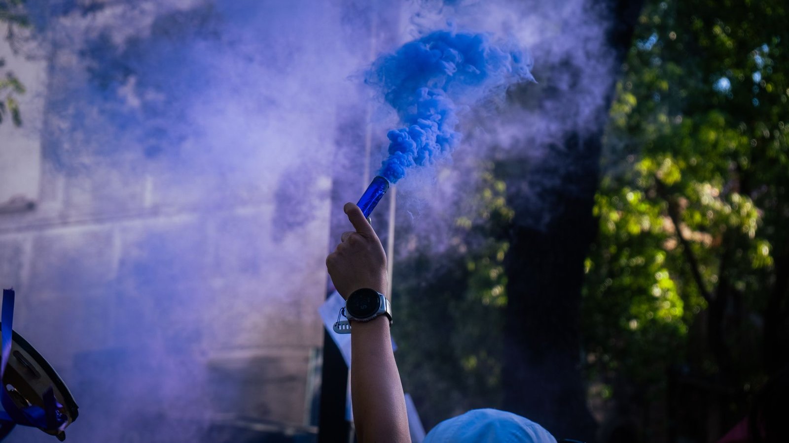 A hand holding a blue smoke flare, creating vibrant smoke in an outdoor setting.
