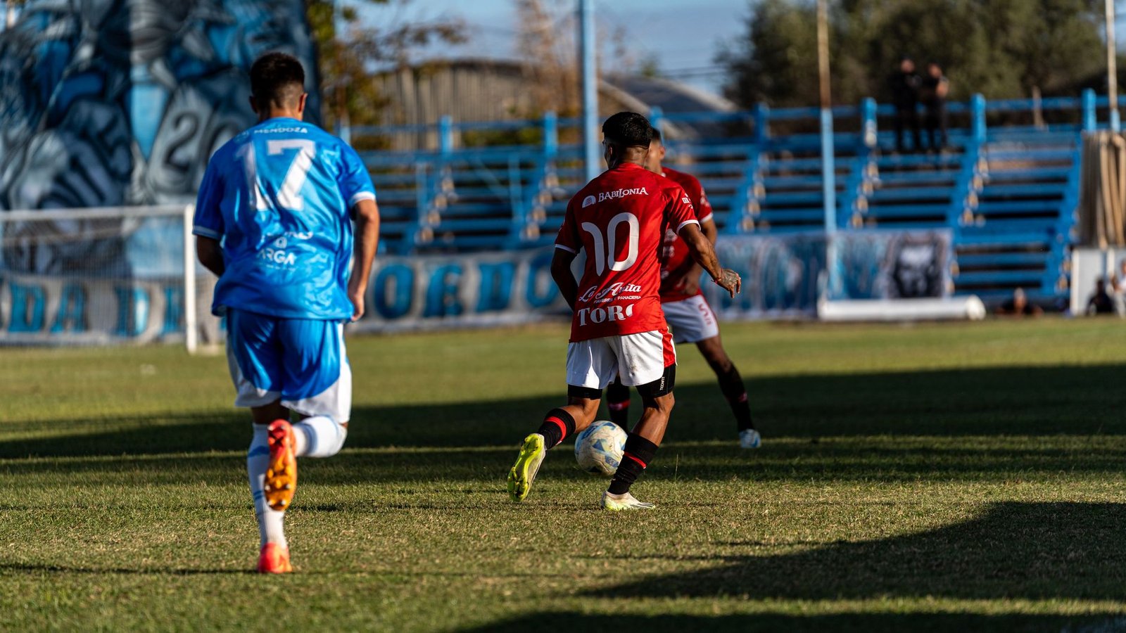 Players in red and blue jerseys competing in a local soccer match outdoors.