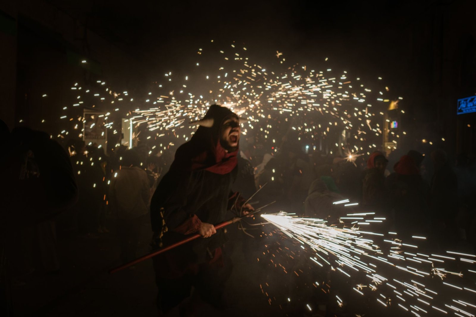 A man in a costume celebrates with sparklers at a vibrant nighttime festival.