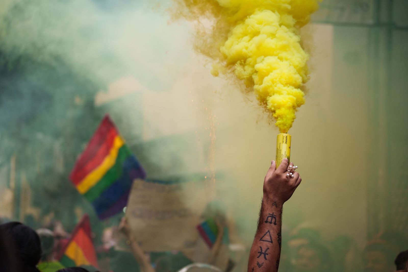 An energetic pride parade with colorful flags and a yellow smoke bomb creating a lively atmosphere.