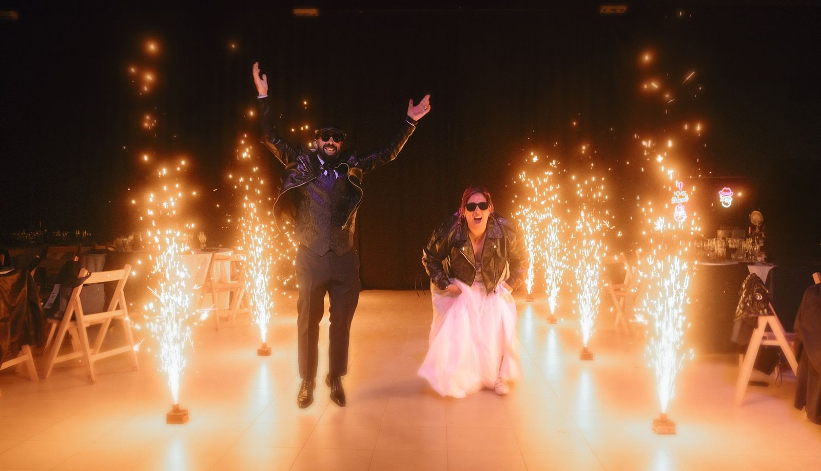 A lively wedding entrance with a couple celebrating amid sparkling fireworks indoors.